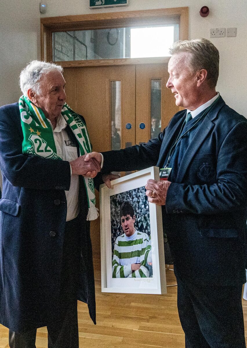 Paddy Mulligan shaking hands indoors at the stadium as he is handed a framed photograph of himself as a young player in the hoops.