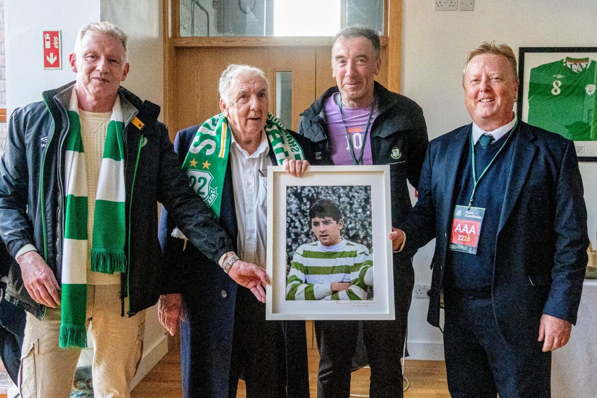 Paddy Mulligan holding his framed photograph, with three other men beside him indoors at the stadium.